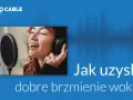 Kobieta w słuchawkach śpiewa do mikrofonu, pokazując jak uzyskać dobrą dynamikę dźwięku.