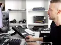 Mężczyzna uczy się produkcji muzyki przy komputerze, otoczony sprzętem: kontrolerami, głośnikami i słuchawkami.