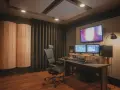 Studio nagraniowe z monitorem studyjnym, dwoma ekranami, wygodnym fotelem i panelami akustycznymi, które pomagają w kontroli **damping factor**.