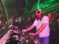DJ w białej koszulce grający na konsoli w klubie z zielonymi laserami.