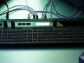 Zielony Korg SQ-64 z podświetlanymi na czerwono przyciskami, otoczony innymi syntezatorami i klawiaturą, tworzy scenę do tworzenia muzyki.
