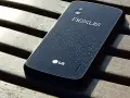 Ciemny tył telefonu LG Nexus 4 z kroplami wody na powierzchni, leżący na drewnianej ławce.