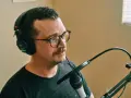 Mężczyzna w okularach i słuchawkach Sony nagrywa podcast. Dba o odpowiedni gain staging, by dźwięk był czysty.