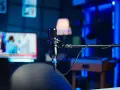 Profesjonalne studio do nagrywania z mikrofonem w centrum. W tle widać ekran telewizora z wiadomościami i niebieskie oświetlenie.