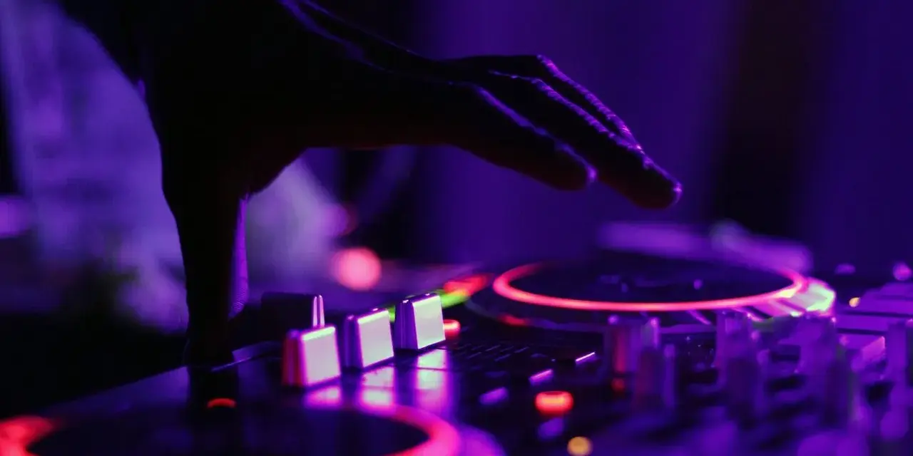 Dłoń DJ-a nad konsolą, czerwone i fioletowe światła. To właśnie tak tworzy się dubstep, co to za muzyka?