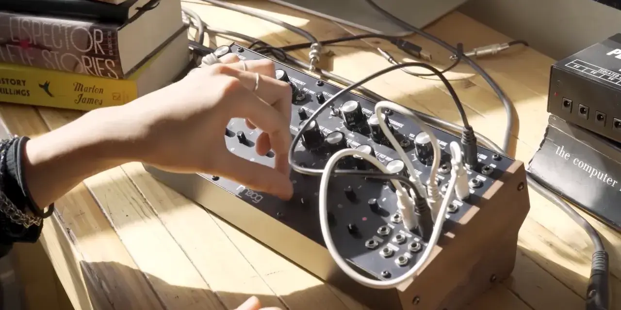 Ręka manipuluje pokrętłami na syntezatorze Moog DFAM, tworząc dźwięki.