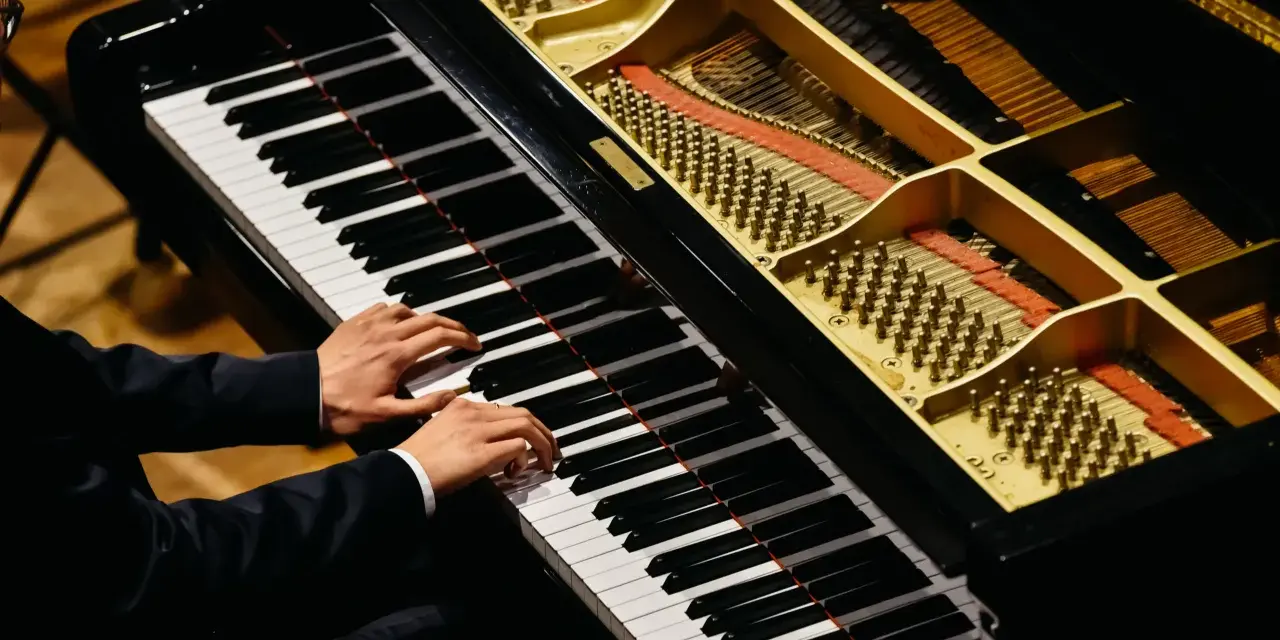 Dłonie muzyka grające na fortepianie, którego wnętrze z widocznymi strunami i młoteczkami przypomina zaawansowany piano vst.