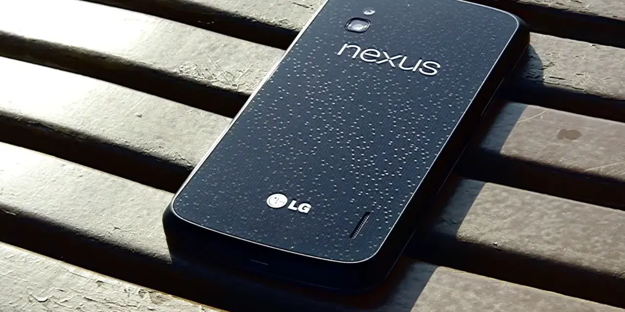 Ciemny tył telefonu LG Nexus 4 z kroplami wody na powierzchni, leżący na drewnianej ławce.