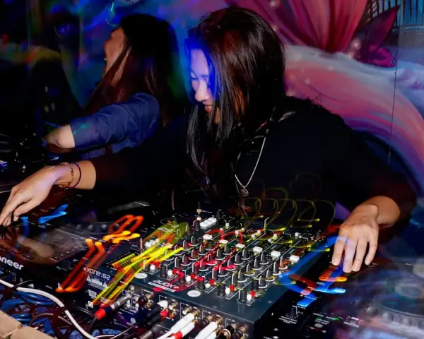 DJka miksuje energetyczne rytmy afro house w klubowej atmosferze. Kolorowe światła i dynamiczna muzyka tworzą niepowtarzalny klimat.