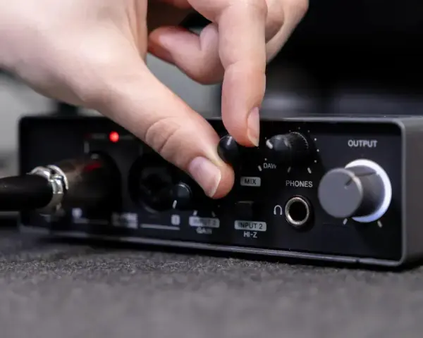 Dłoń reguluje pokrętło miksu na interfejsie audio, przygotowując wyjście liniowe do pracy.