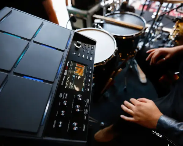 Nowoczesny sampler perkusyjny Roland SPD-SX PRO gotowy do tworzenia rytmów. W tle widoczne elementy zestawu perkusyjnego.