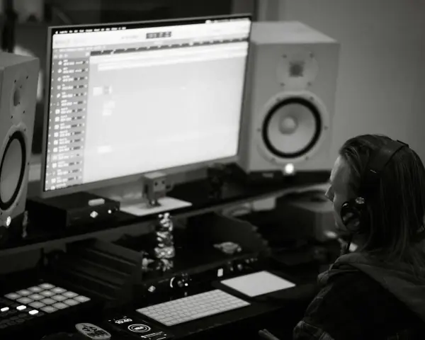 Producent muzyczny w słuchawkach tworzy beaty w studiu. Zastanawia się, czym się różni trap od rapu, analizując dźwięki na monitorze.