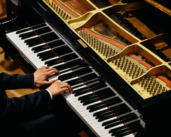 Dłonie muzyka grające na fortepianie, którego wnętrze z widocznymi strunami i młoteczkami przypomina zaawansowany piano vst.