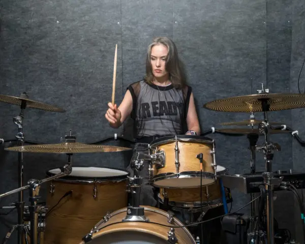 Kobieta z pałeczką w dłoni, gotowa do wygenerowania mocnych **drum beats** na zestawie perkusyjnym w studio.