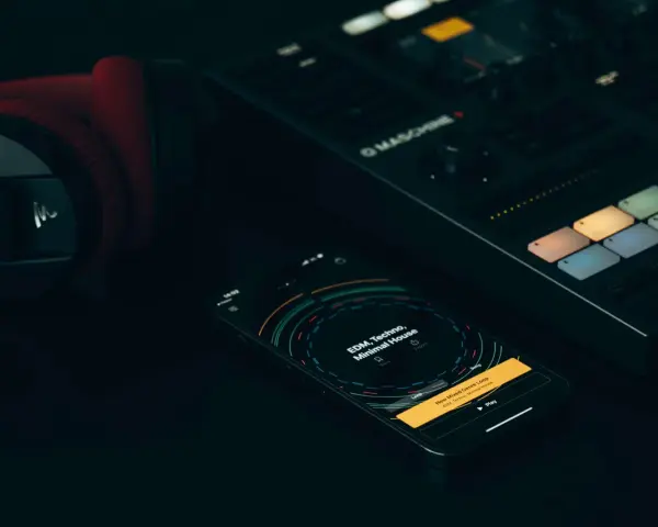 Czerwone słuchawki, kontroler Maschine i smartfon z aplikacją do tworzenia muzyki, gdzie widać koala sampler.