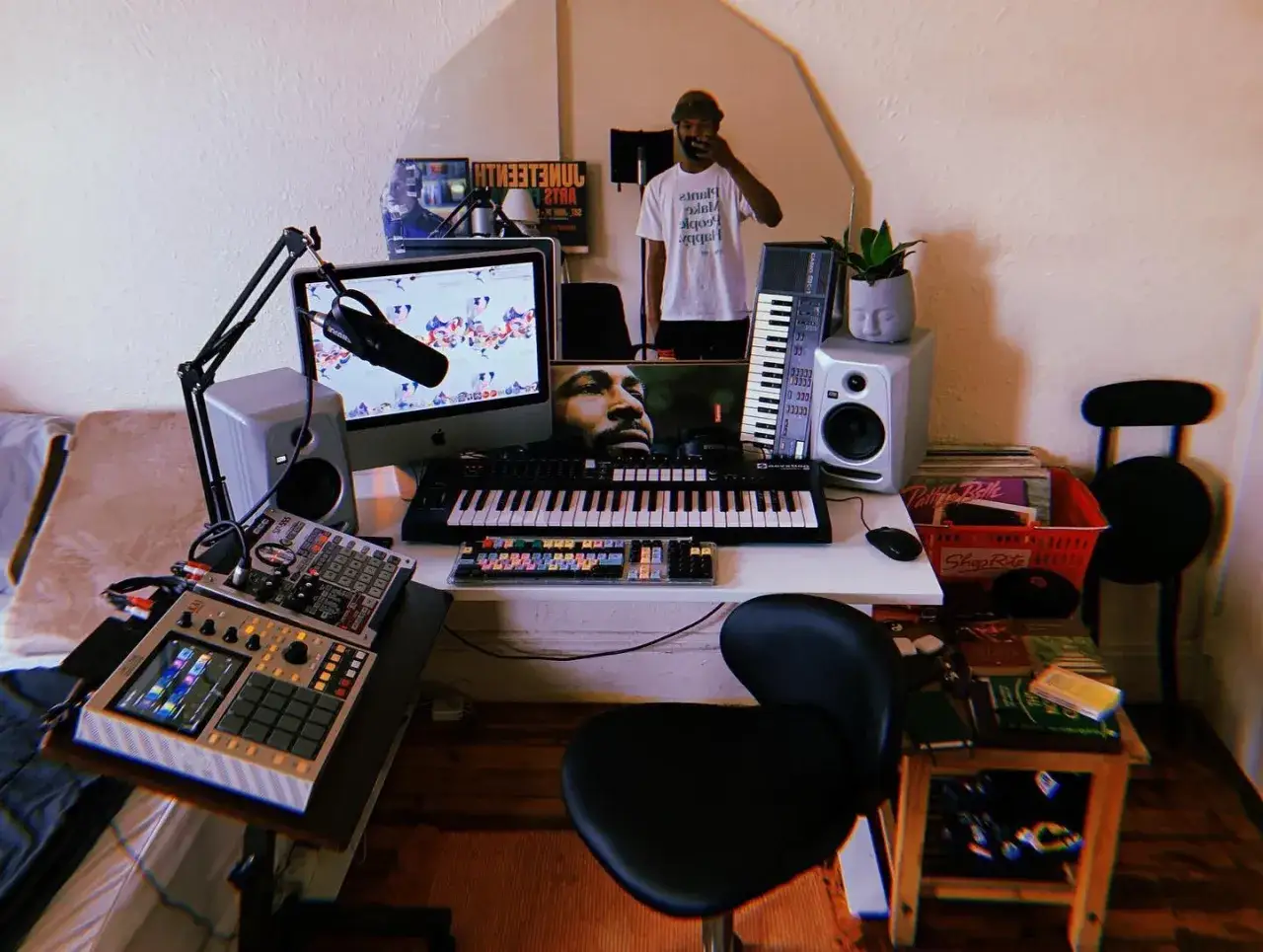 Pokój muzyka z komputerem, klawiaturami, samplerem i mikrofonem. W lustrze odbija się twórca, tworzący w stylu low fi.