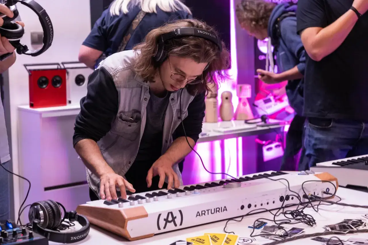 Młody mężczyzna w słuchawkach gra na keyboardzie Arturia. Wokół leżą kable i inne akcesoria muzyczne, tworząc scenę dla tworzenia music stems.