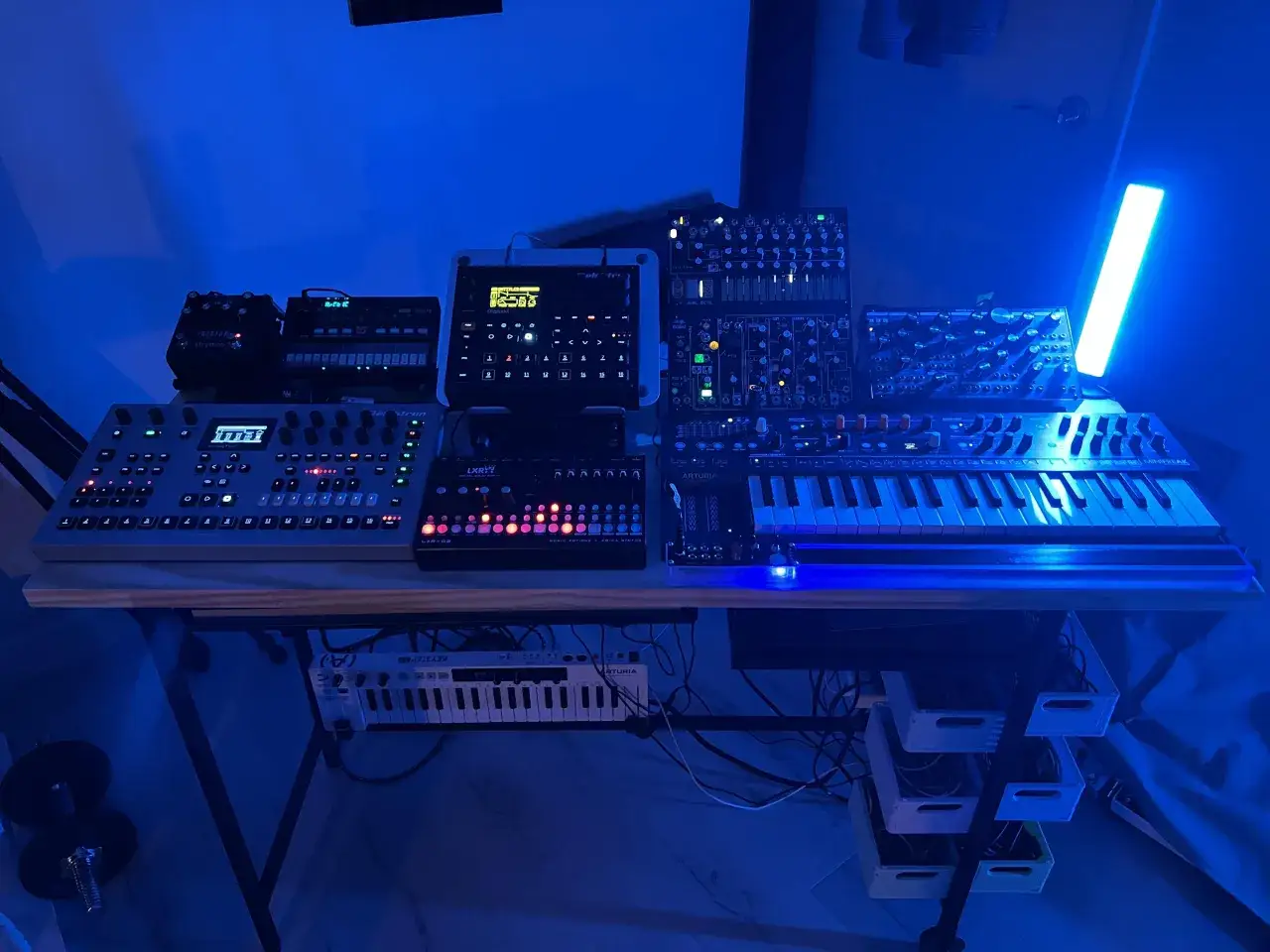 Stół z syntezatorami i kontrolerami, w tym sprzęt od Soma Laboratory, w niebieskim świetle.